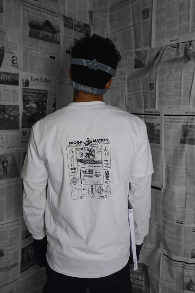 Image du T-shirt avec illustration de Journal des Sorties 2023 de la Collection Programation d'Amble : Une personne de dos portant ce t-shirt dans une salle remplie de journaux. Explorez la rétrospective de l'année.